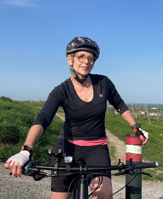 Nahaufnahme einer Person beim Rad fahren. Die Person lächelt in die Kamera.