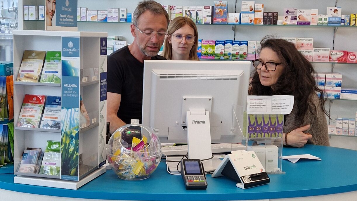 Drei Personen stehen am Apothekenpult mit Sicht auf den PC.