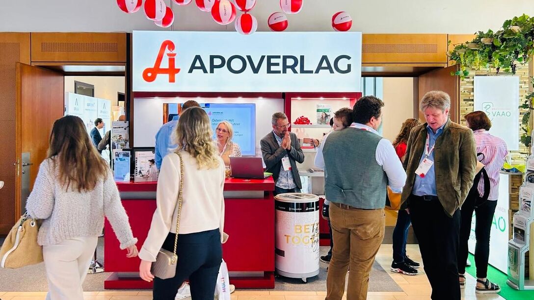 Nahaufnahme des APOVERLAG-Messestand beim APOkongress in Pörtschach 2024 mit den Besucherinnen und Besuchern. Es werden angeregte Gespräche geführt.