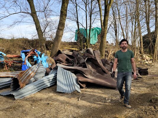 Jan Dansa blickt in die Kamera. Hinter ihm ist Müll, der aus den Flüssen entfernt wurde, zu sehen. 